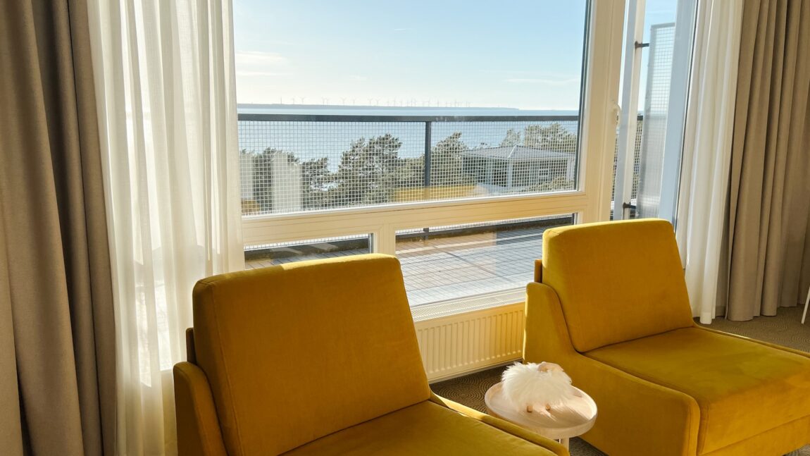 LaSpa suite with yellow lounge chairs by large window, balcony and sea view, soft natural light and calm Nordic interior